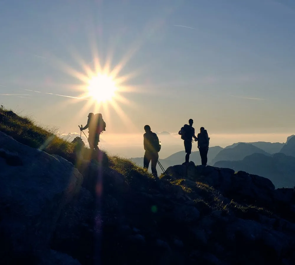Four hikers silhouetted on a rocky ridge against a rising sun.