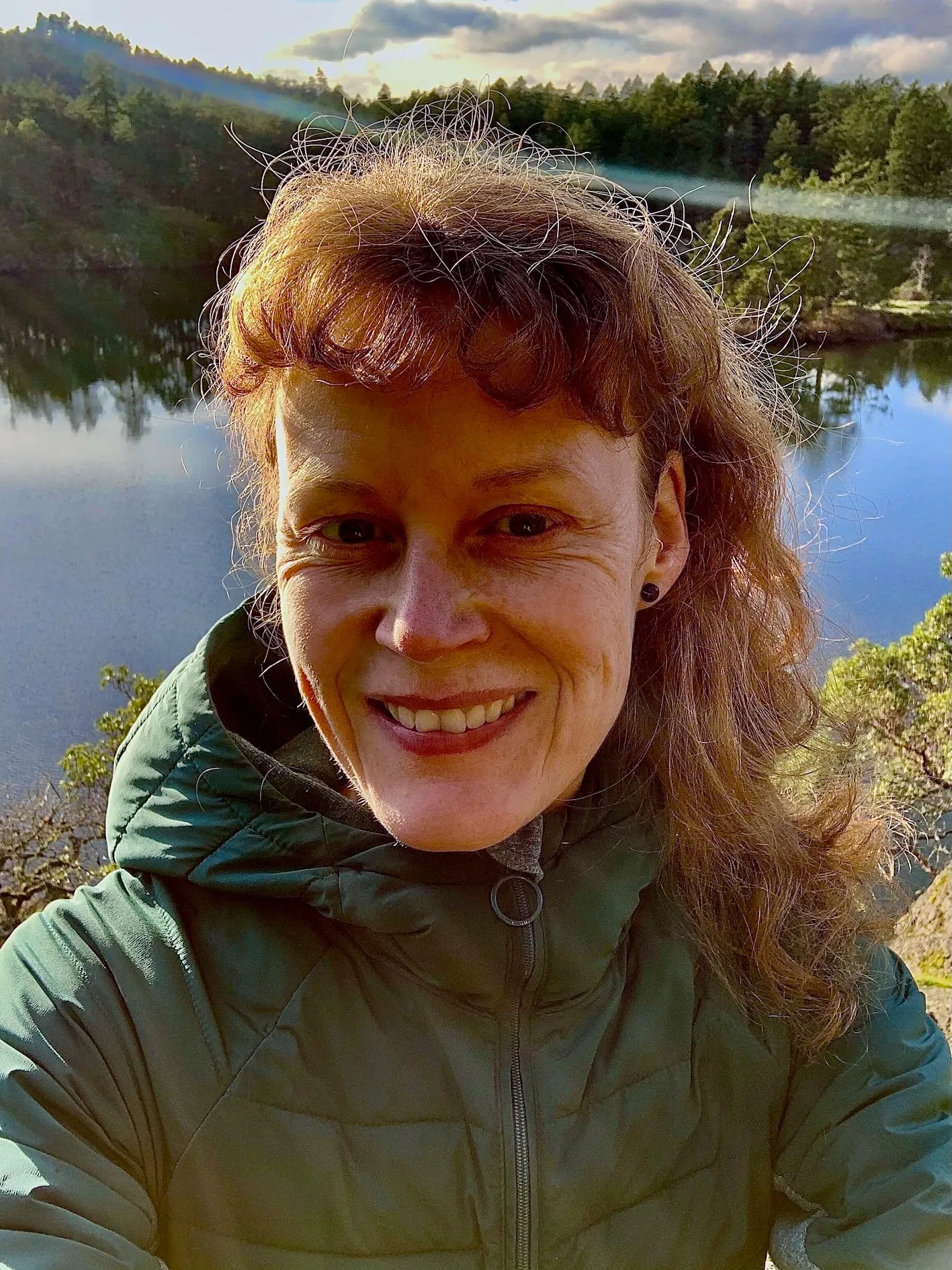 Alysha Jones smiling outdoors in a green jacket, a lake behind her.
