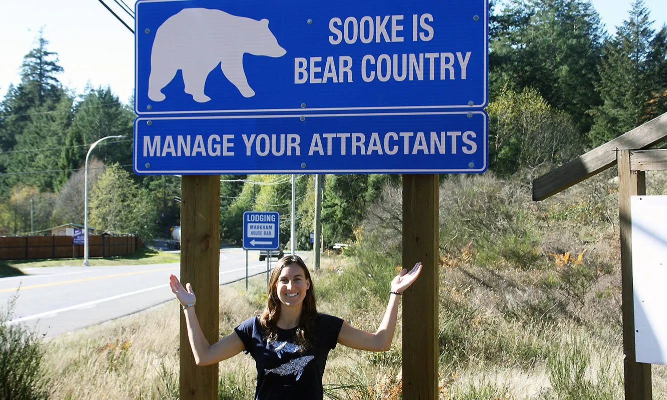 Sam Webb standing under a road sign reading Sooke is bear country, manage your attractants.