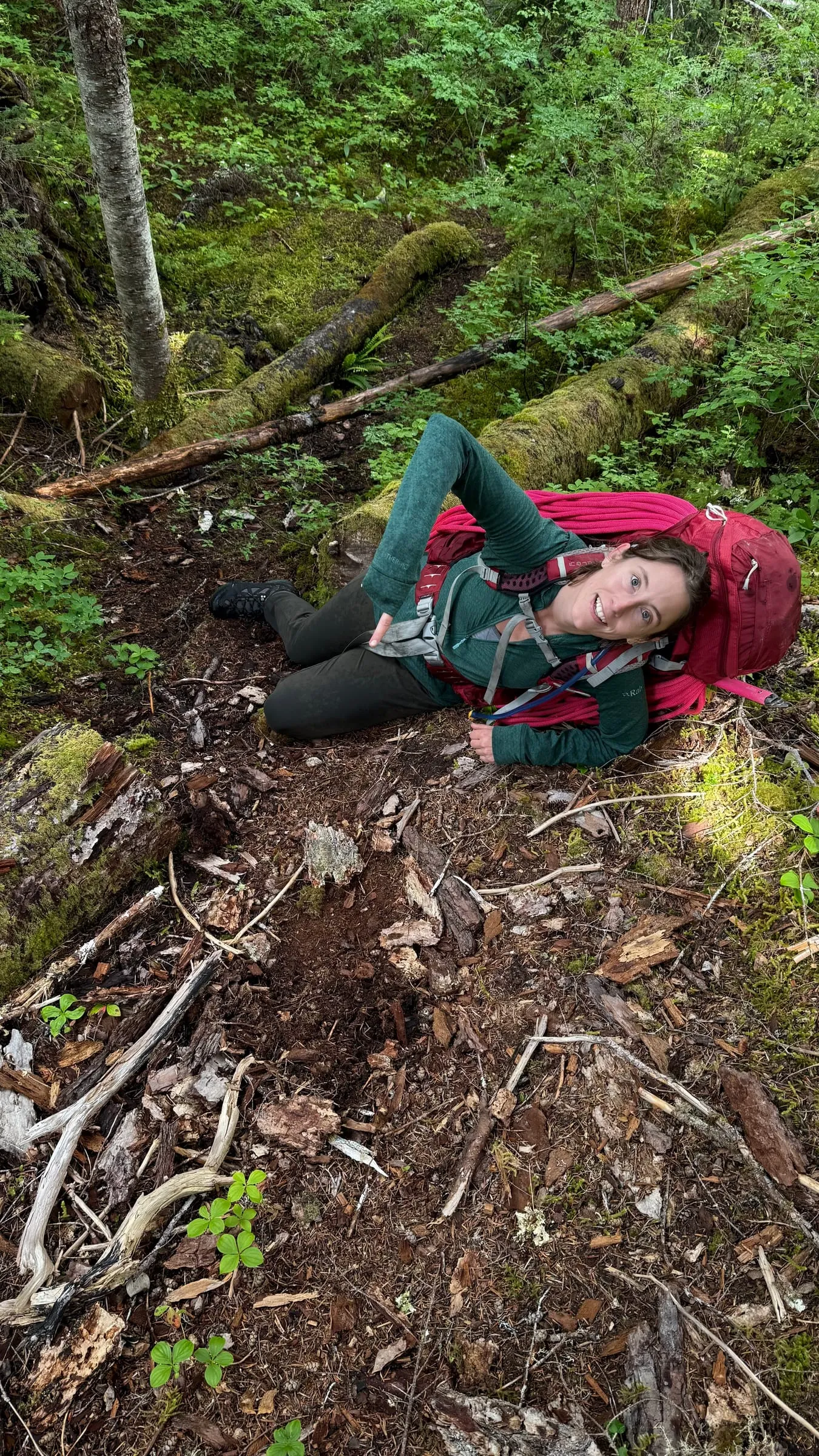 Shannon Hamilton lying on a mossy forest slope beside a backpack, smiling.