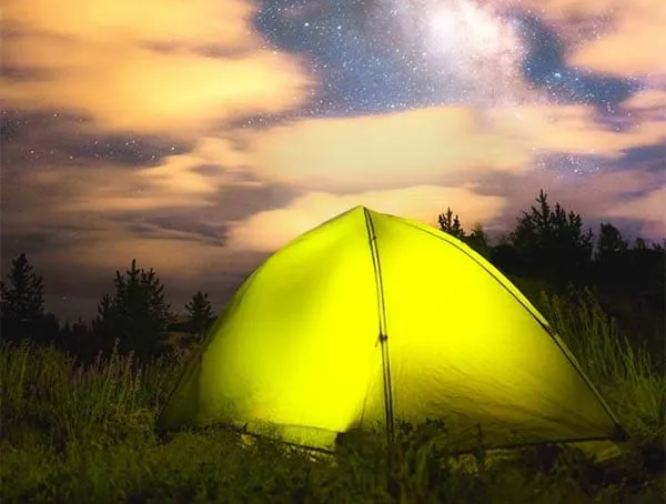 A lit tent glowing yellow-green under a starry night sky.
